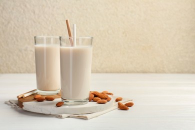 Photo of Glasses of almond milk and almonds on white wooden table, space for text