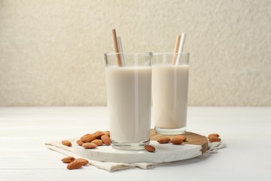 Glasses of almond milk and almonds on white wooden table