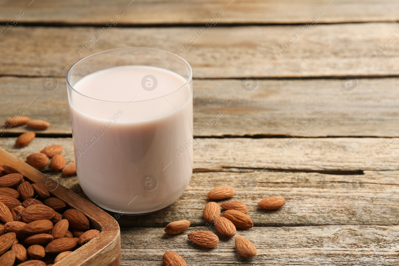 Photo of Glass of almond milk and almonds on wooden table, space for text