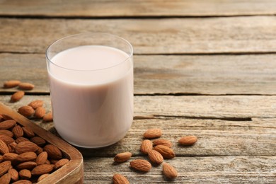 Glass of almond milk and almonds on wooden table, space for text