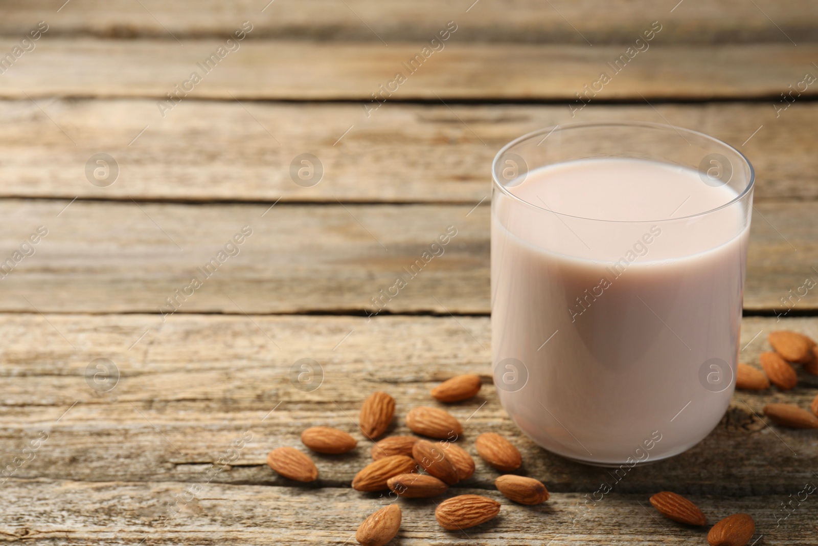 Photo of Glass of almond milk and almonds on wooden table, space for text