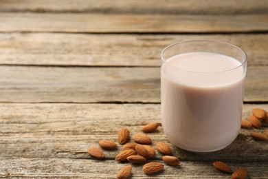 Glass of almond milk and almonds on wooden table, space for text