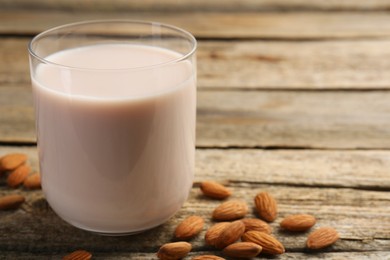 Photo of Glass of almond milk and almonds on wooden table, space for text