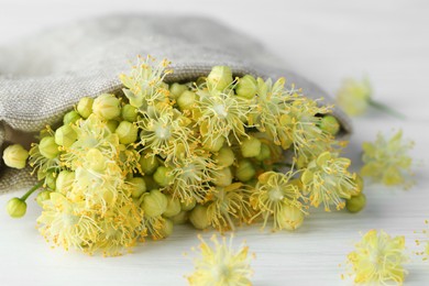 Fresh linden leaves and flowers in bag on white wooden table, closeup