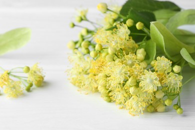 Photo of Fresh linden leaves and flowers on white wooden table, closeup