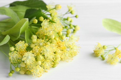 Photo of Fresh linden leaves and flowers on white wooden table, closeup