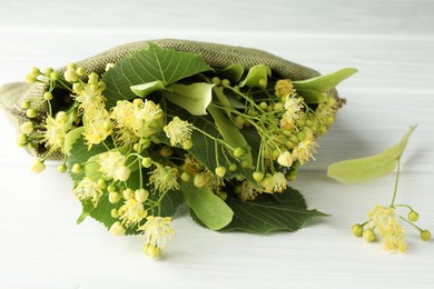 Fresh linden leaves and flowers on white wooden table, closeup