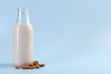 Fresh almond milk in glass bottle and nuts on light blue background, space for text