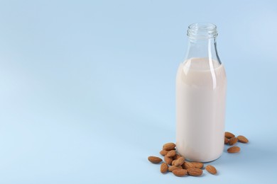 Fresh almond milk in glass bottle and nuts on light blue background, space for text