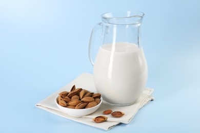 Photo of Fresh almond milk in glass jug and nuts on light blue background