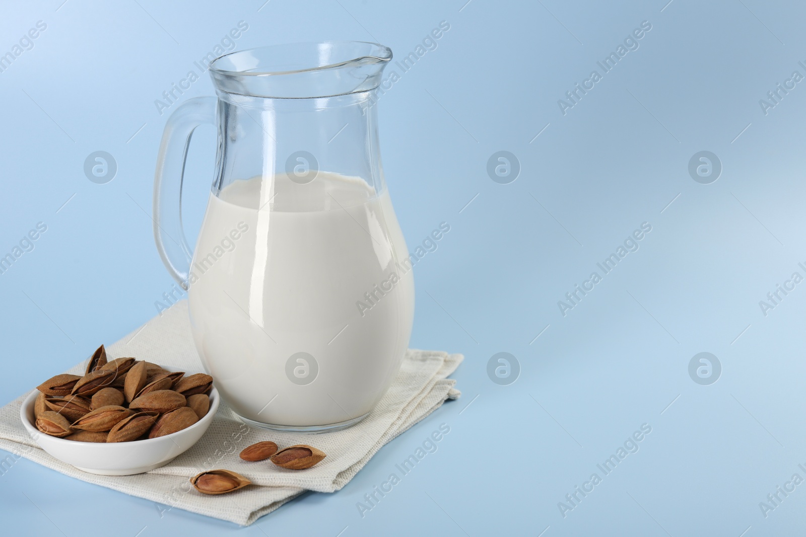 Photo of Fresh almond milk in glass jug and nuts on light blue background, space for text