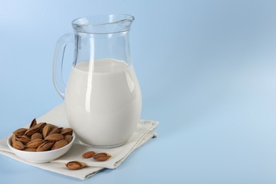 Fresh almond milk in glass jug and nuts on light blue background, space for text