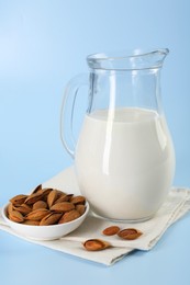 Fresh almond milk in glass jug and nuts on light blue background