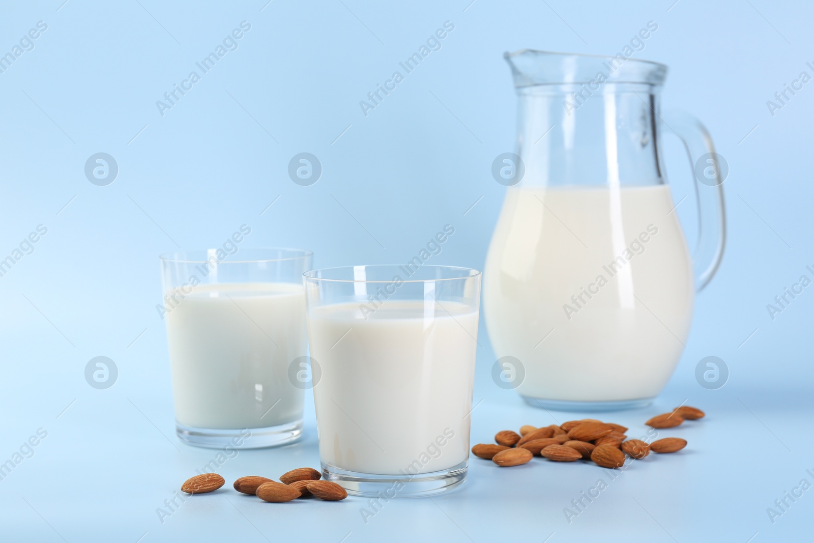 Photo of Fresh almond milk in glasses, jug and nuts on light blue background