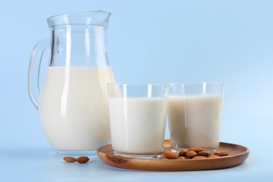 Fresh almond milk in glasses, jug and nuts on light blue background