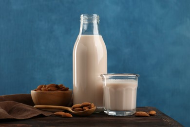 Fresh almond milk in bottle, glass, nuts and spoon on wooden table