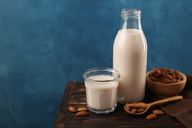 Fresh almond milk in bottle, glass, nuts and spoon on wooden table, space for text