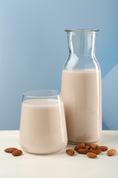 Photo of Fresh almond milk in carafe, glass and nuts on white wooden table