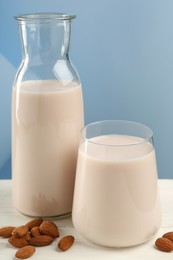 Fresh almond milk in carafe, glass and nuts on white wooden table