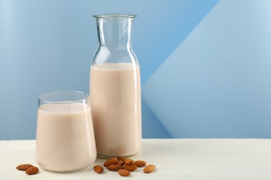 Photo of Fresh almond milk in carafe, glass and nuts on white wooden table, space for text