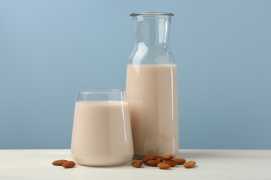 Fresh almond milk in carafe, glass and nuts on white wooden table