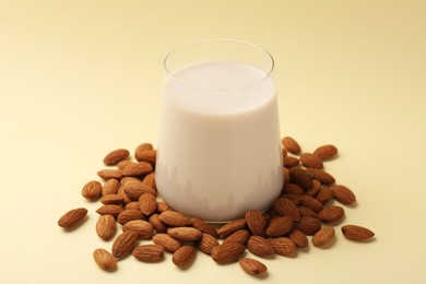 Fresh almond milk in glass and nuts on beige background