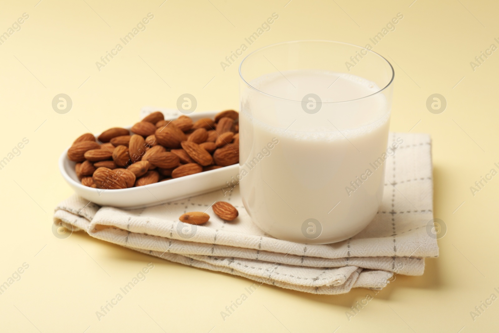 Photo of Fresh almond milk in glass and nuts on beige background