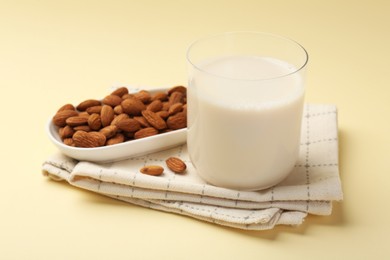 Fresh almond milk in glass and nuts on beige background