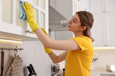 Professional janitor wearing uniform cleaning cabinet in kitchen