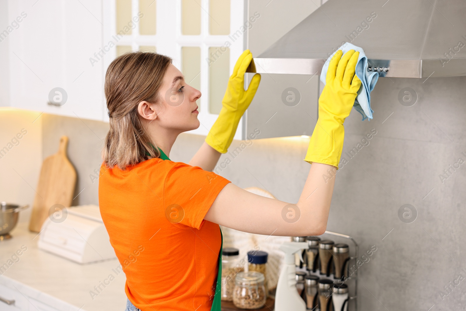 Photo of Professional janitor wearing uniform cleaning kitchen hood with rag indoors