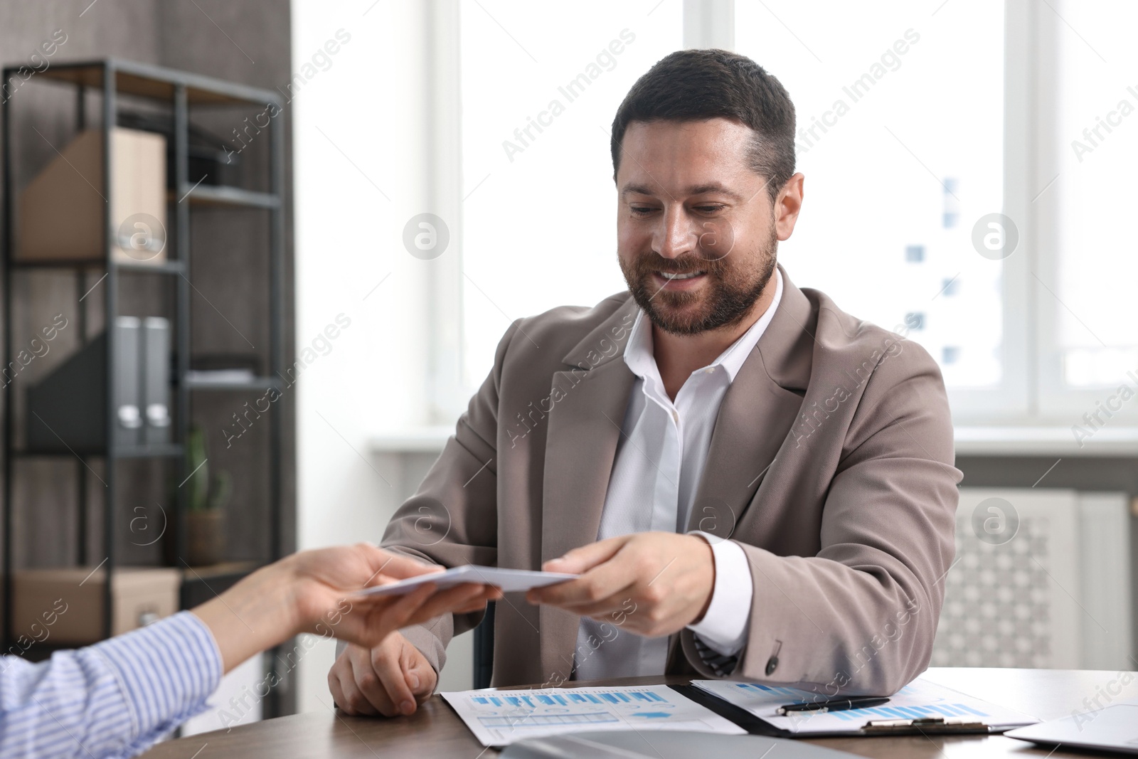 Photo of Boss giving salary in paper envelope to employee indoors