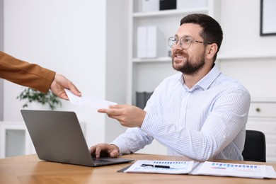 Photo of Boss giving salary in paper envelope to employee indoors