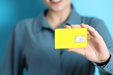 Photo of Woman holding SIM card on light blue background, closeup