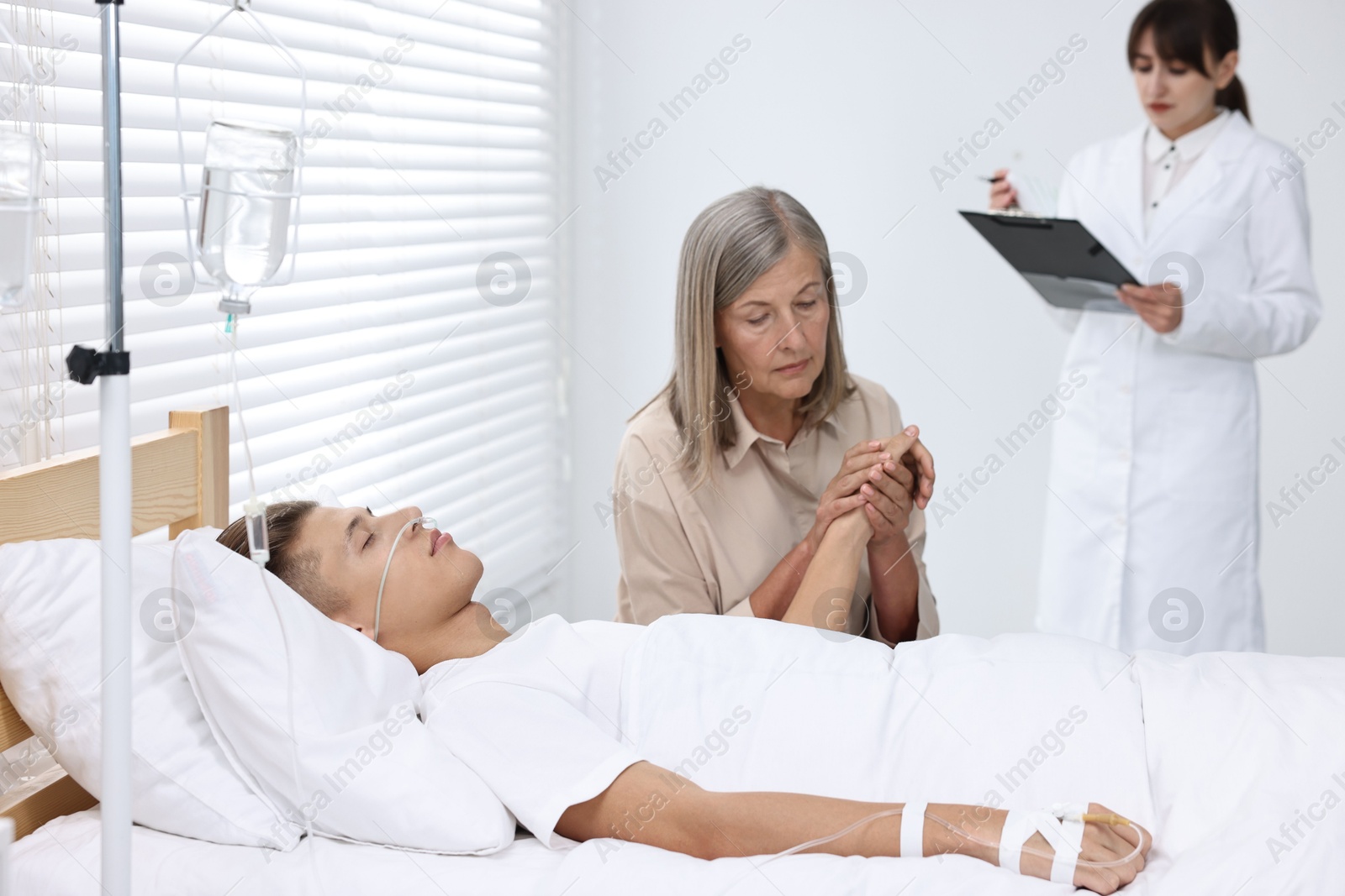 Photo of Coma patient. Sad mature woman near her unconscious son in hospital