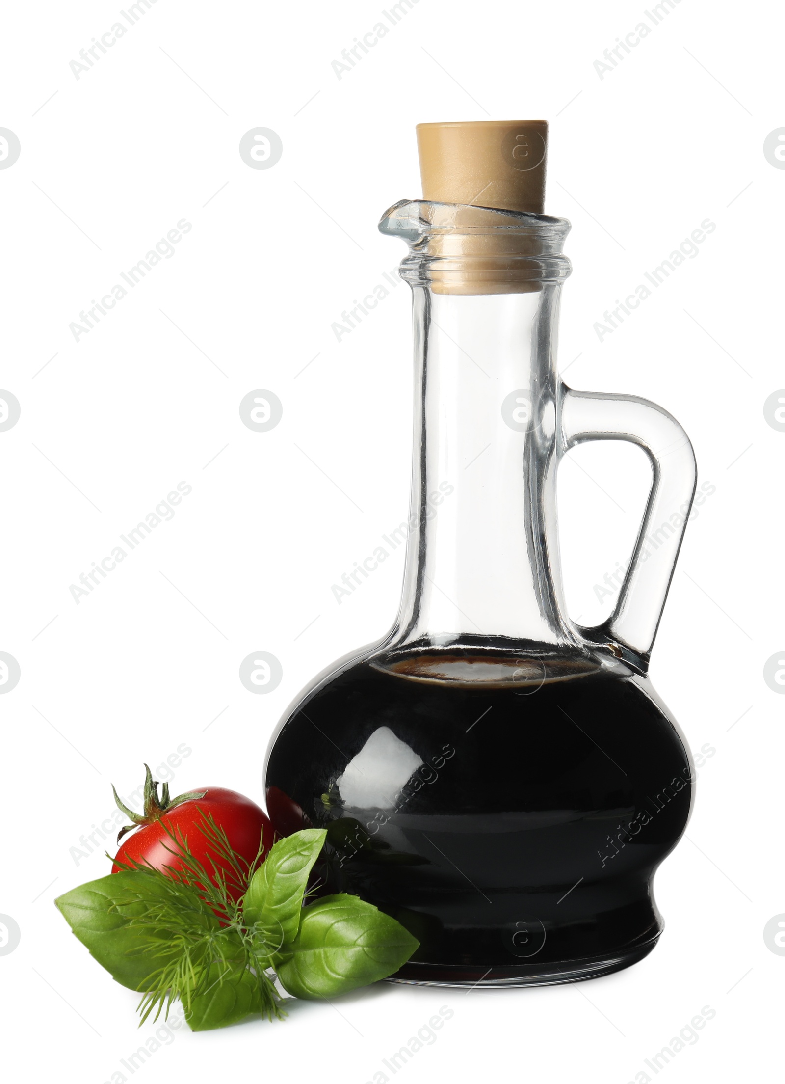 Photo of Balsamic vinegar in glass jug, herbs and tomato isolated on white