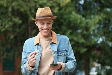 Photo of Happy man with SIM cards and smartphone outdoors, space for text