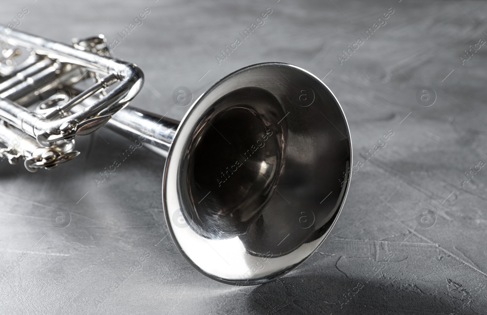 Photo of Closeup view of shiny trumpet on grey textured table. Wind musical instrument