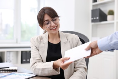Photo of Smiling employee receiving envelope with salary from boss in office