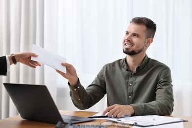 Photo of Smiling employee receiving envelope with salary from boss in office