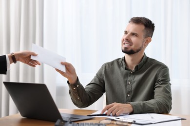 Smiling employee receiving envelope with salary from boss in office