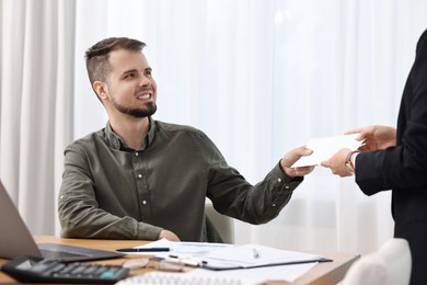 Photo of Smiling employee receiving envelope with salary from boss in office