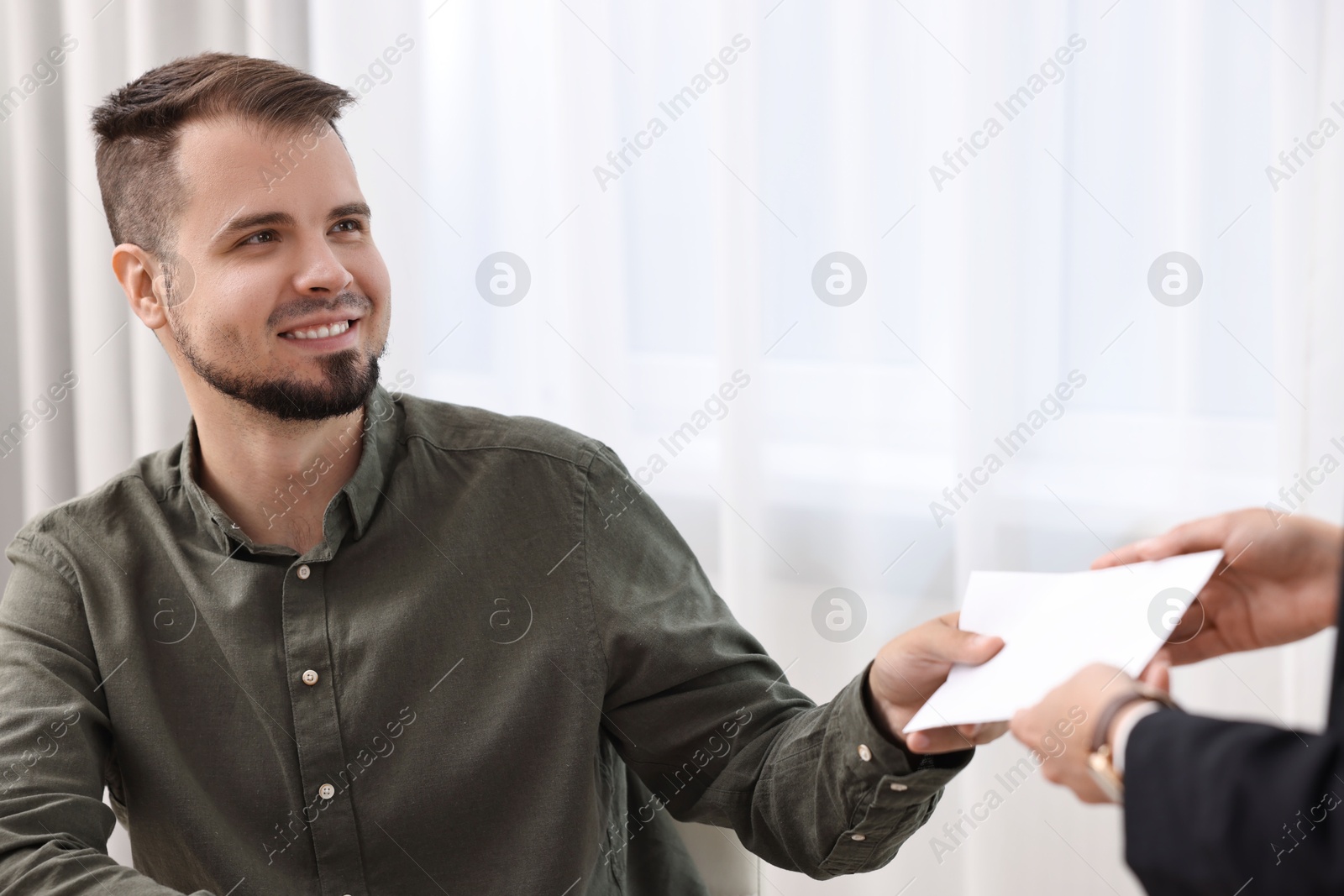 Photo of Smiling employee receiving envelope with salary from boss in office