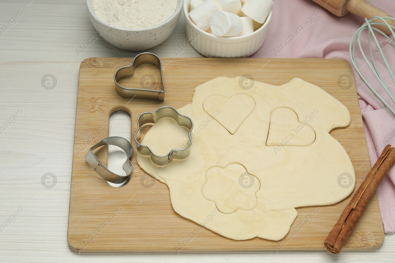 Photo of Raw dough, cookie cutters and flour on white wooden table, above view