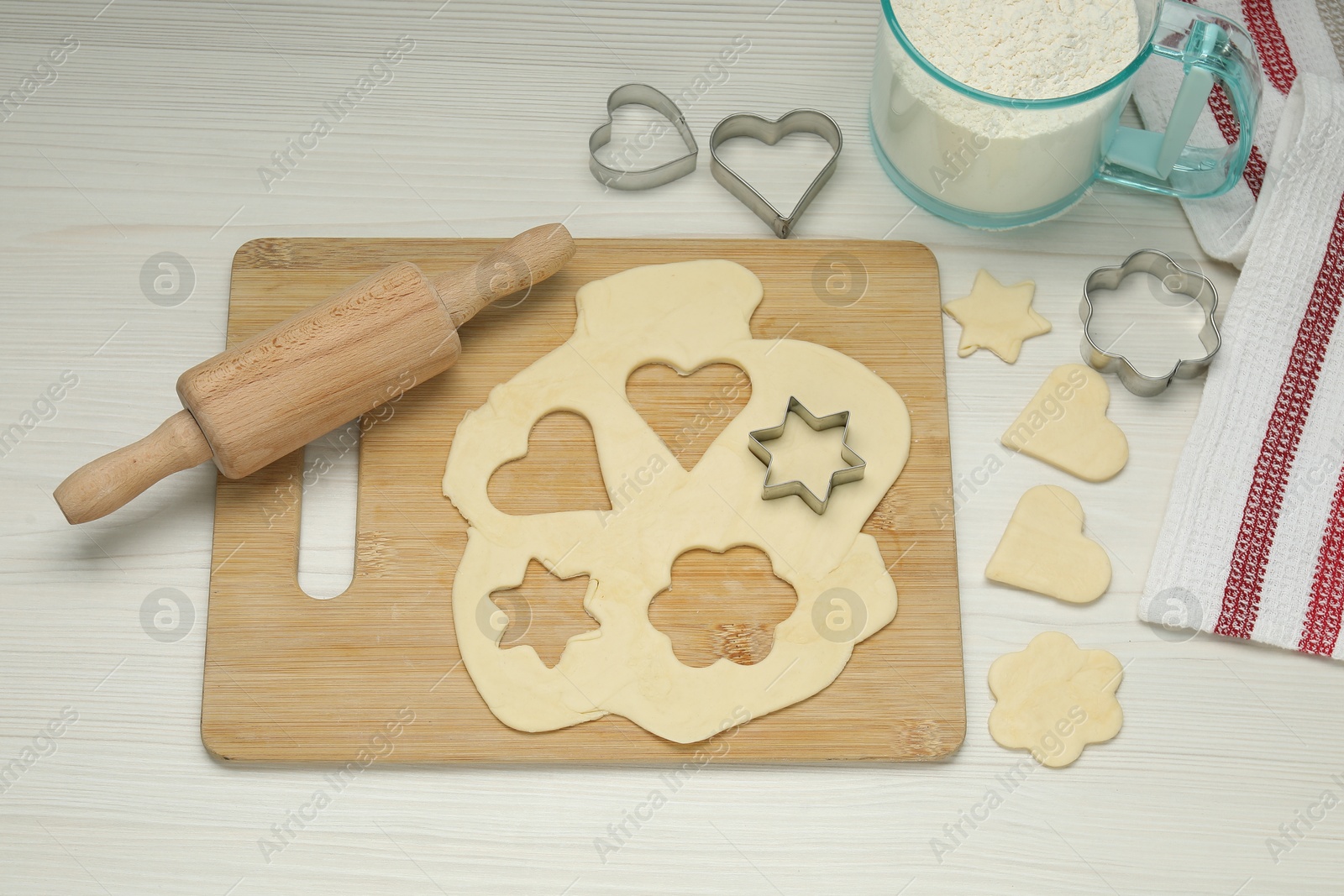 Photo of Raw dough, cookie cutters, rolling pin and flour on white wooden table, above view