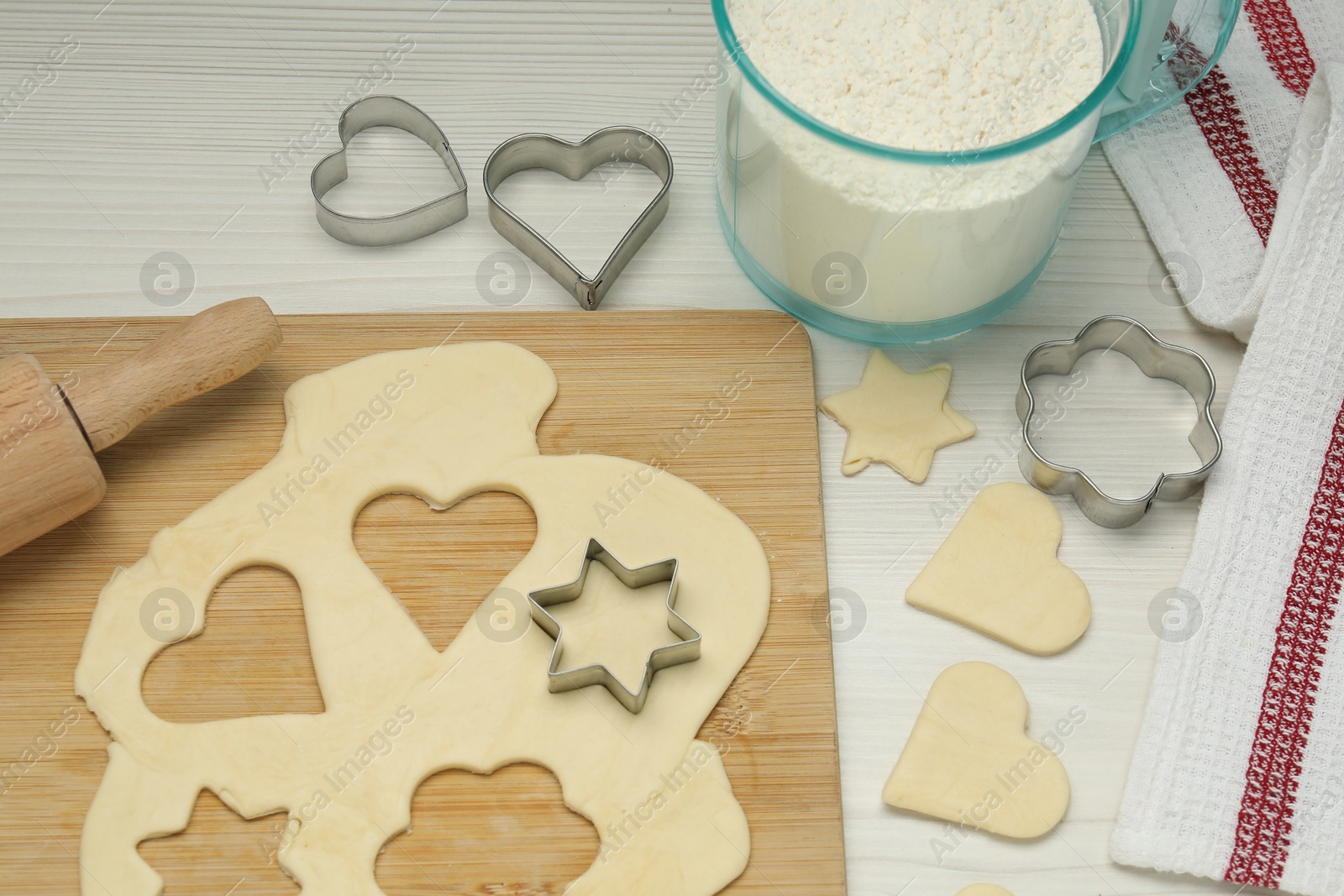 Photo of Raw dough, cookie cutters, rolling pin and flour on white wooden table, above view