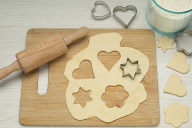 Raw dough, cookie cutters, rolling pin and flour on white wooden table, above view