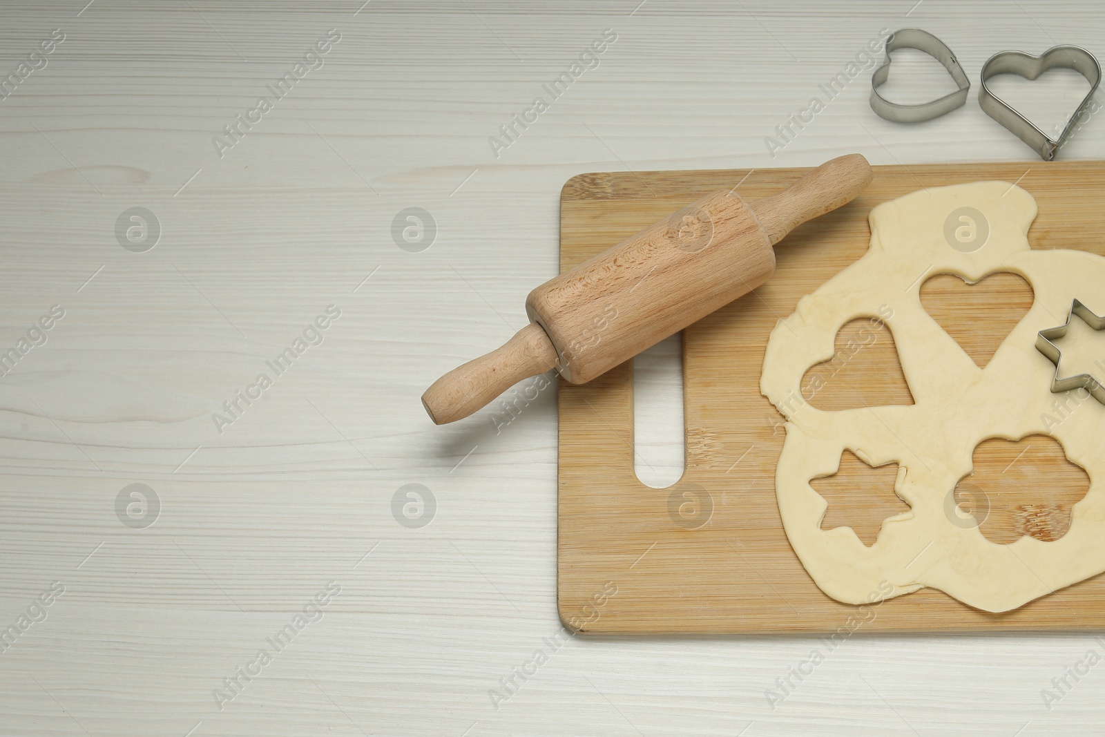 Photo of Raw dough, cookie cutters and rolling pin on white wooden table, above view. Space for text