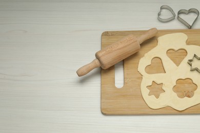 Raw dough, cookie cutters and rolling pin on white wooden table, above view. Space for text