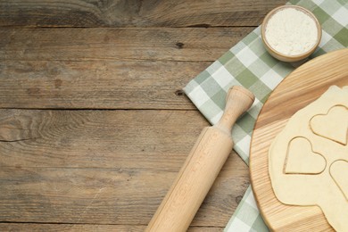 Raw dough, rolling pin and flour on wooden table, flat lay. Space for text