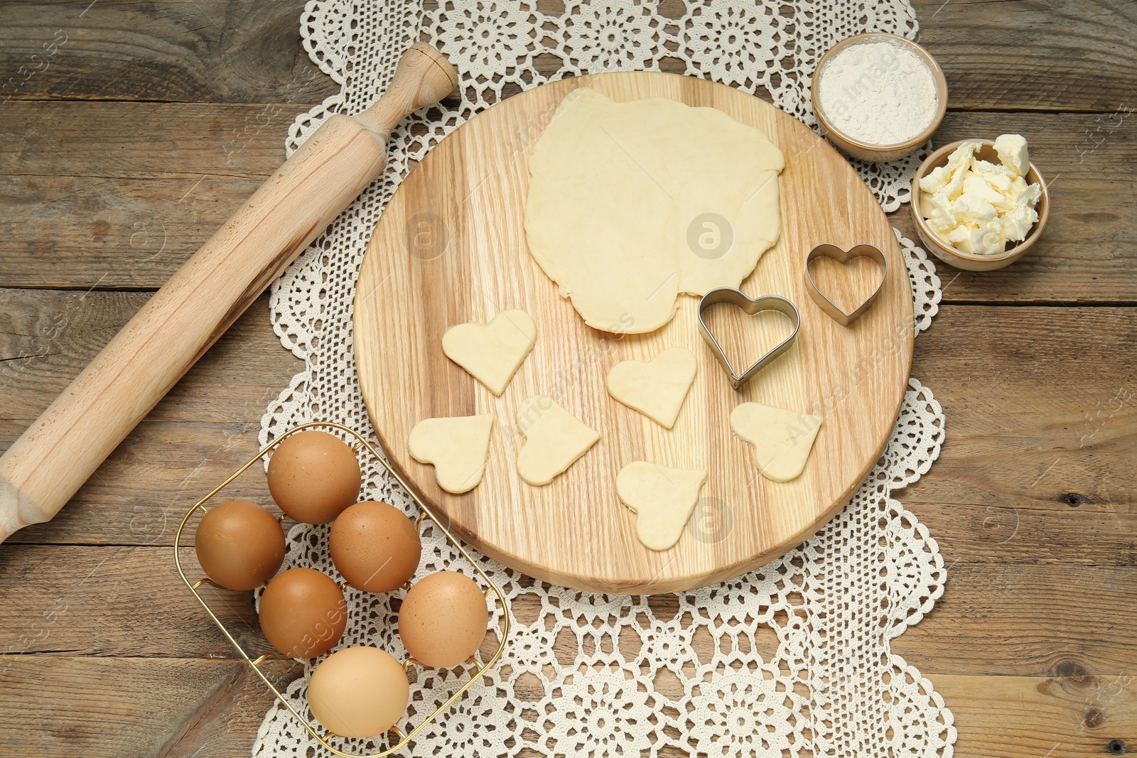 Photo of Raw dough, cookie cutters, rolling pin and eggs on wooden table, above view